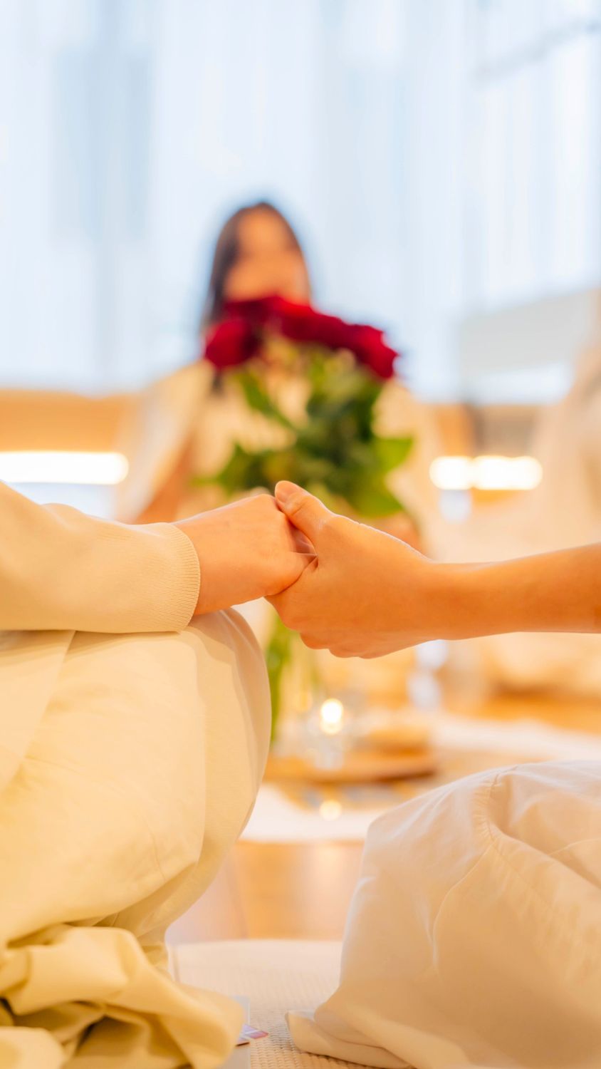 向かい合って手を取り合う二人の女性。奥に赤いバラ